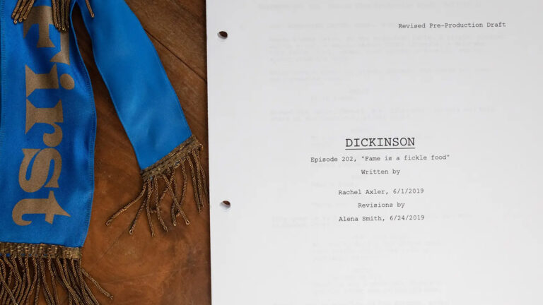 A prop blue ribbon and script for the second episode of Season 2, in which Dickinson’s black cake won first prize at a cattle fair. (Harvard owns her batter-stained handwritten recipe.) Credit...Matt Cosby for The New York Times